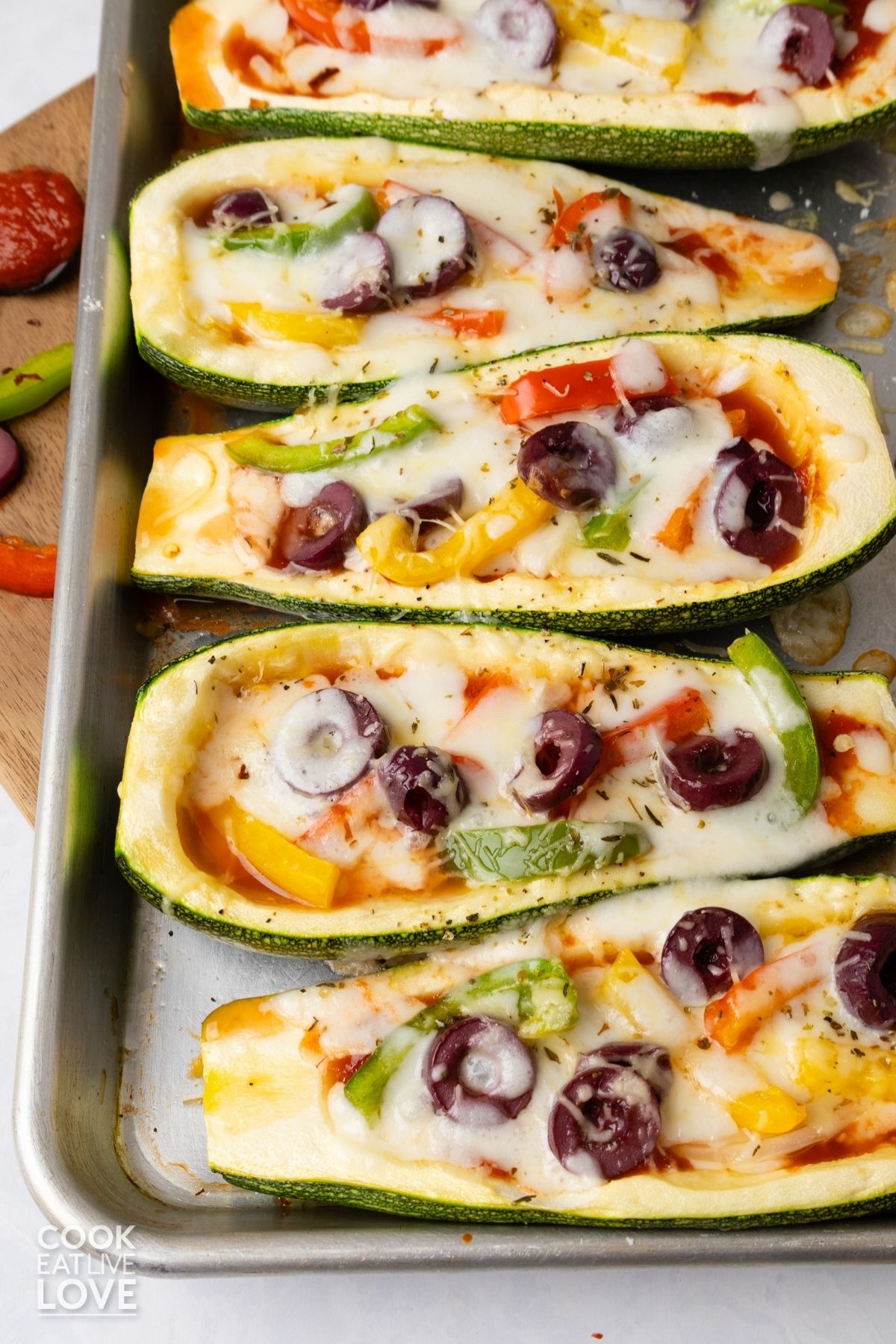 Zucchini pizza boats with vegetables and cheese on a metal sheet pan.