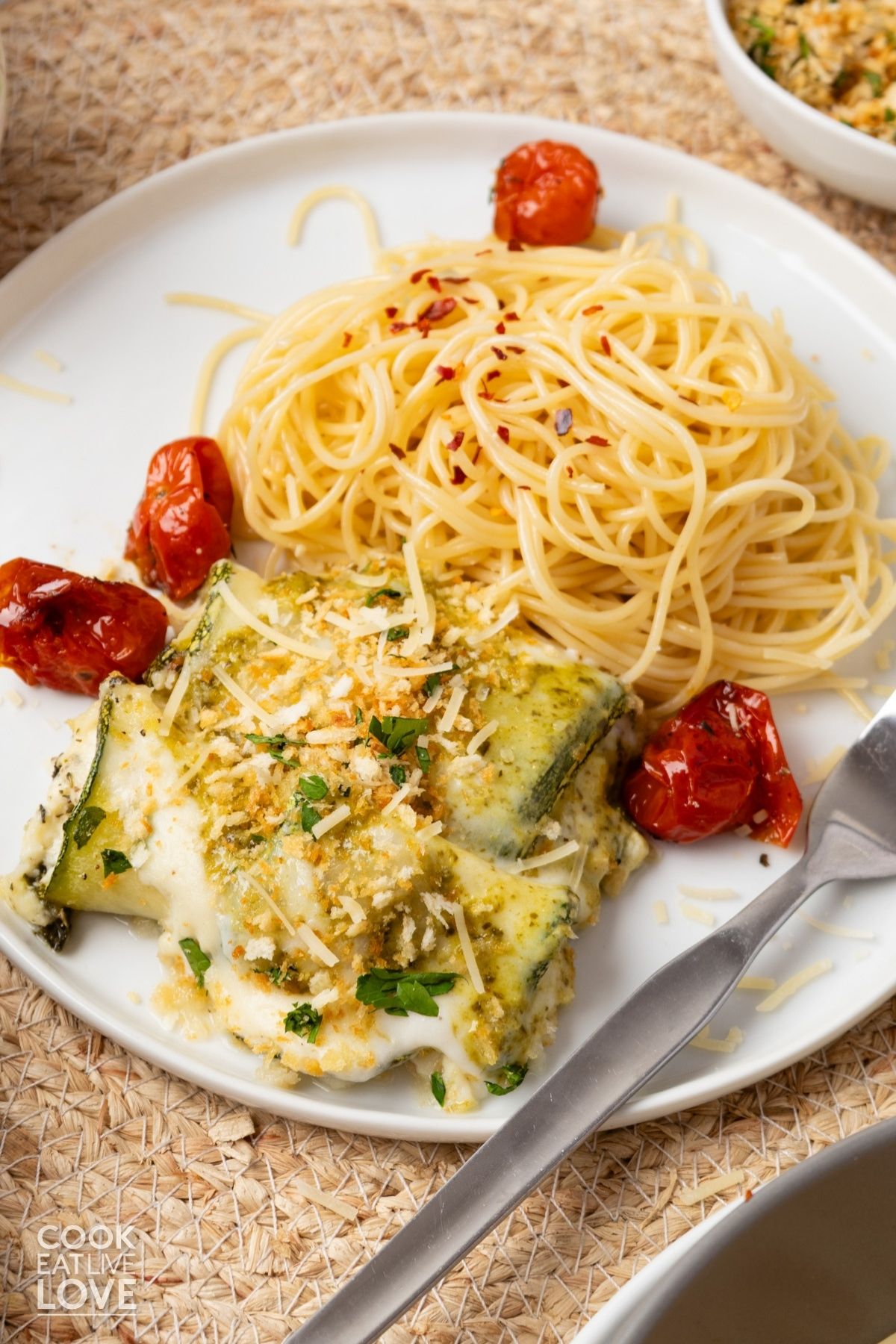 Zucchini rollatini on a plate with spaghetti noodles and a fork to the side.