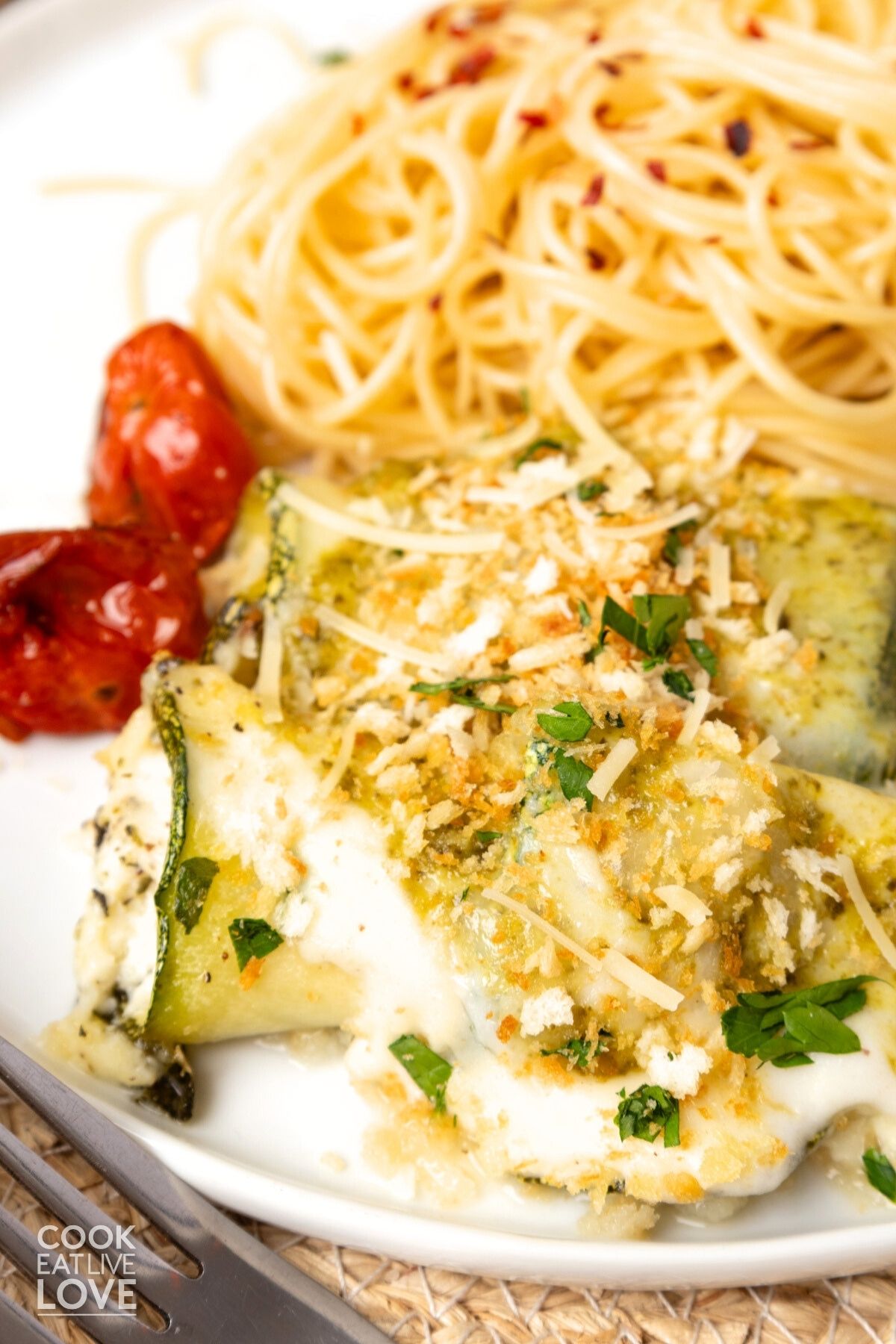 Zucchini rollatini on a plate garnished with shredded parmesan and roasted tomatoes.