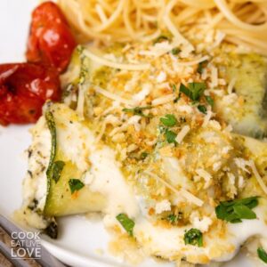 Zucchini rollatini on a plate with roasted tomatoes.