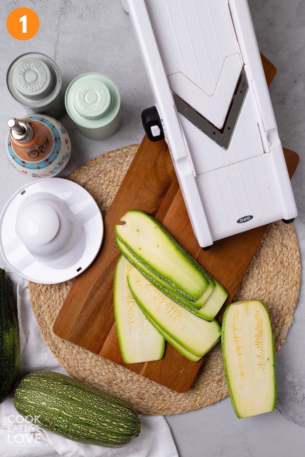 Zucchini sliced on a cutting board with a mandolin to the side.