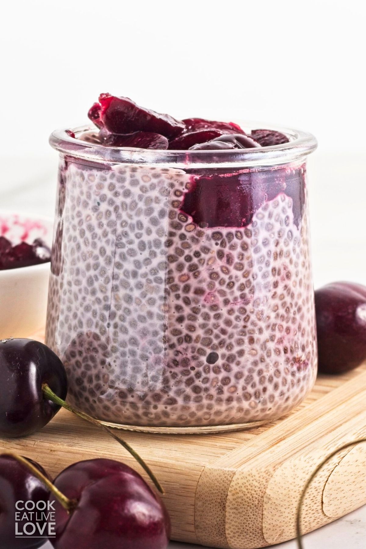A jar of pink chia pudding topped with cherries on top.