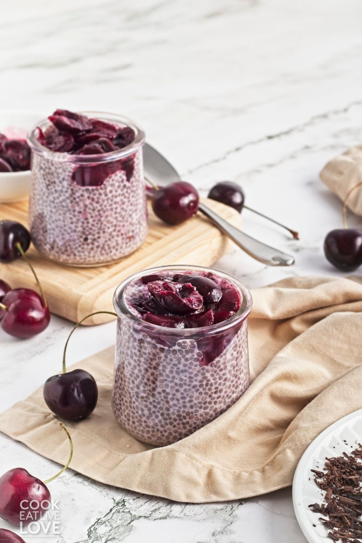 Two jars of cherry chia pudding with fresh cherries scattered around.