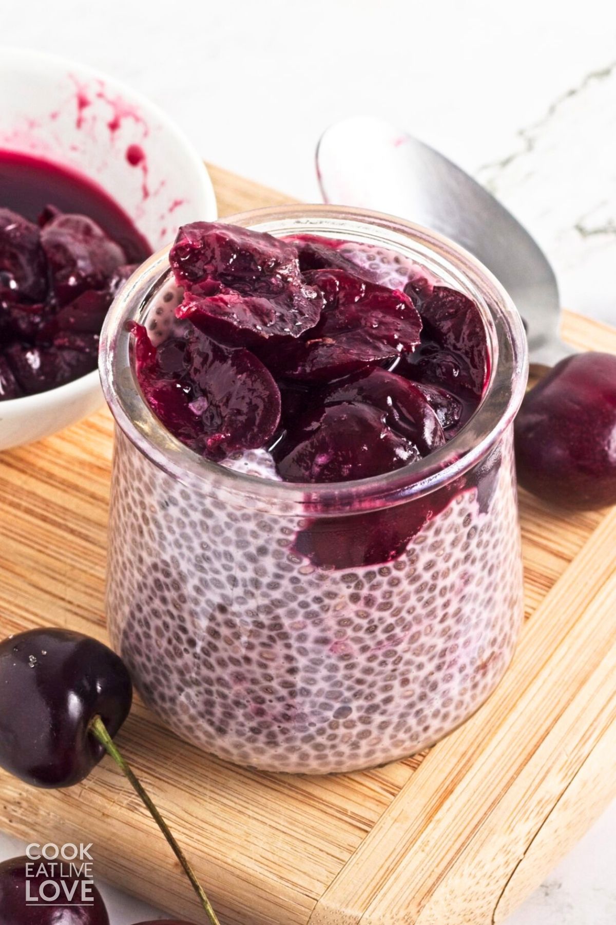 Jar of cherry chia pudding with a bowl of cherry compote in the background.