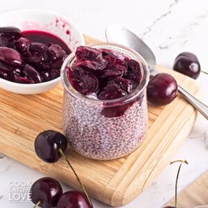 A jar of cherry chia pudding with cherries around it.