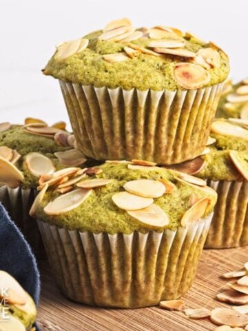 Matcha muffins stacked on top of each other with almonds sprinkled around.