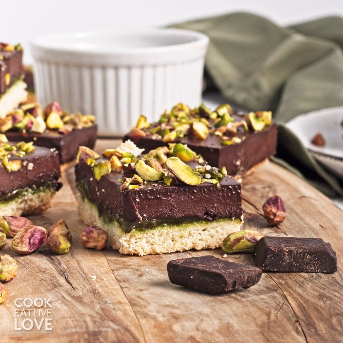 A pistachio bar on a wooden platter with dark chocolate chunks and pistachios scattered around.
