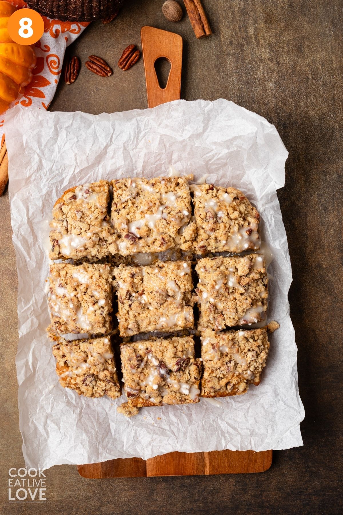 Pumpkin coffee cake cut into squares on a piece of parchment with glaze drizzled over the top.