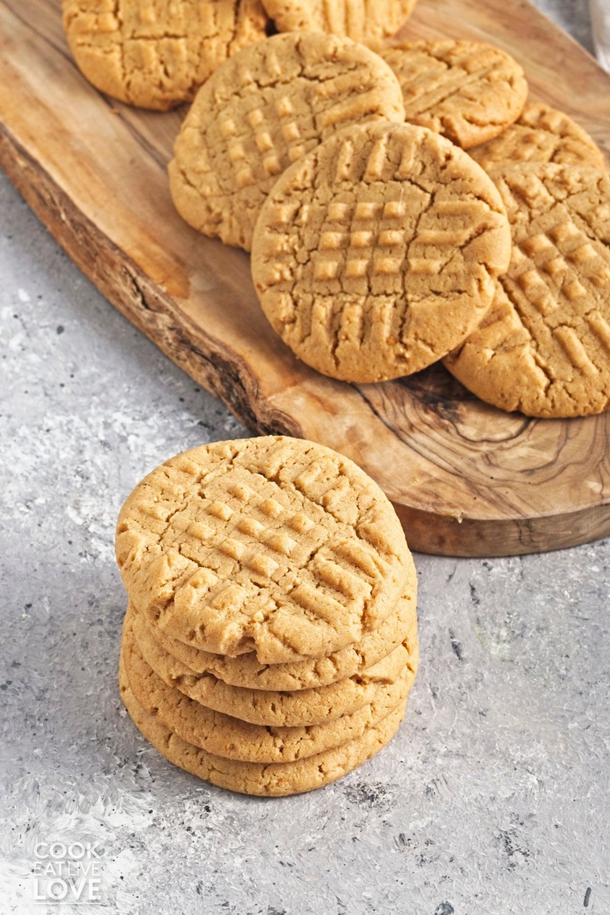 A stack of vegan peanut butter cookies in front of more piled up on a wooden board. 