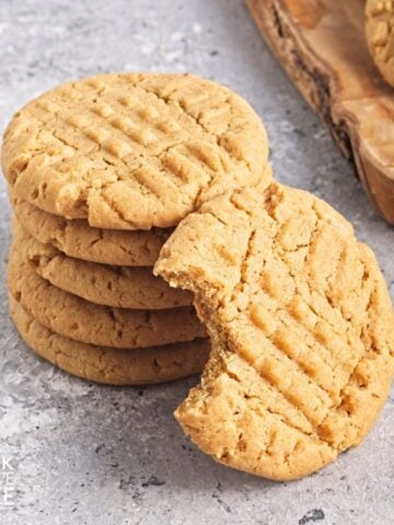 A stack of vegan peanut butter cookies with one resting against it with a bite missing.
