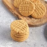 Four vegan peanut butter cookies stacked with more in a pile in the background.