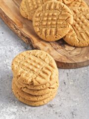 Four vegan peanut butter cookies stacked with more in a pile in the background.