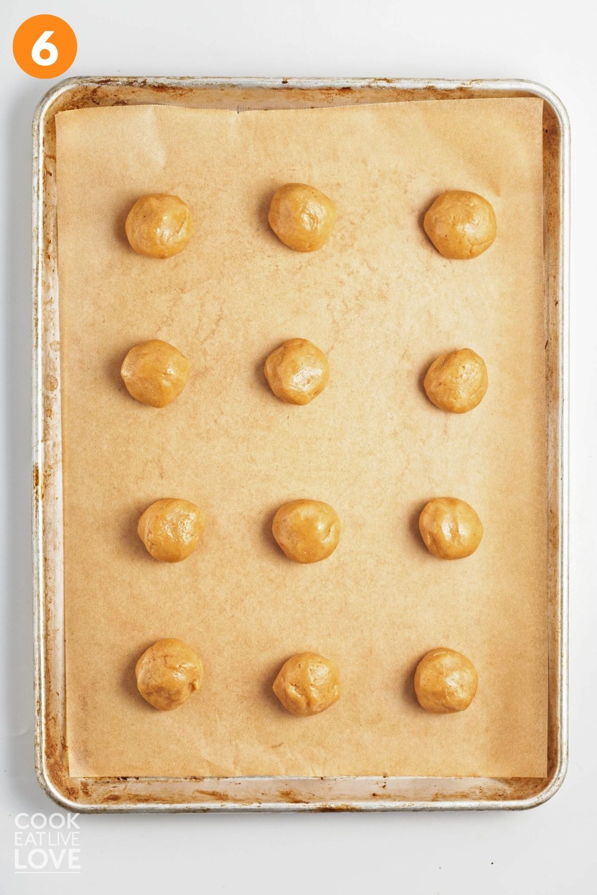 Balls of peanut butter cookie dough on a parchment lined baking sheet.