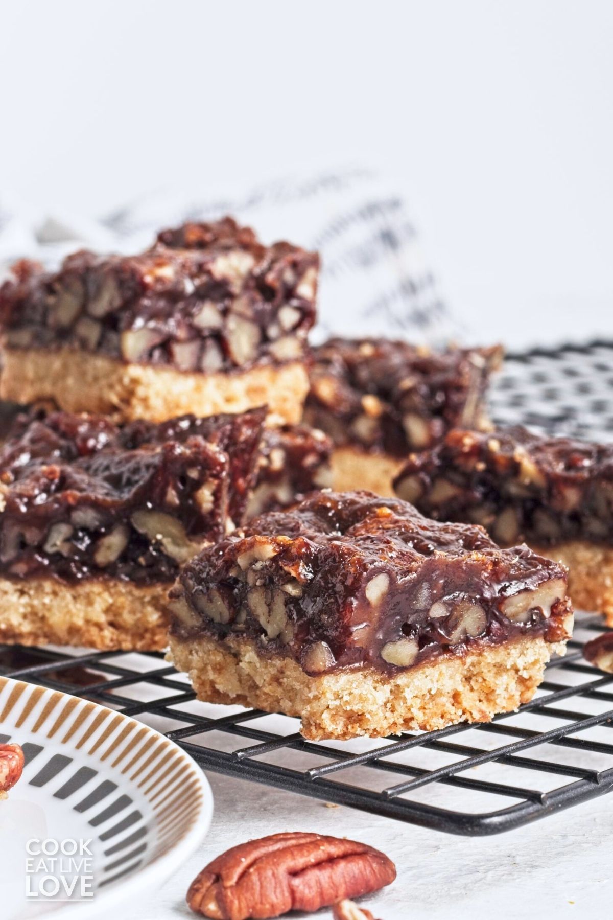 Pecan bars cut into squares and stacked on top of each other on a cooling rack.