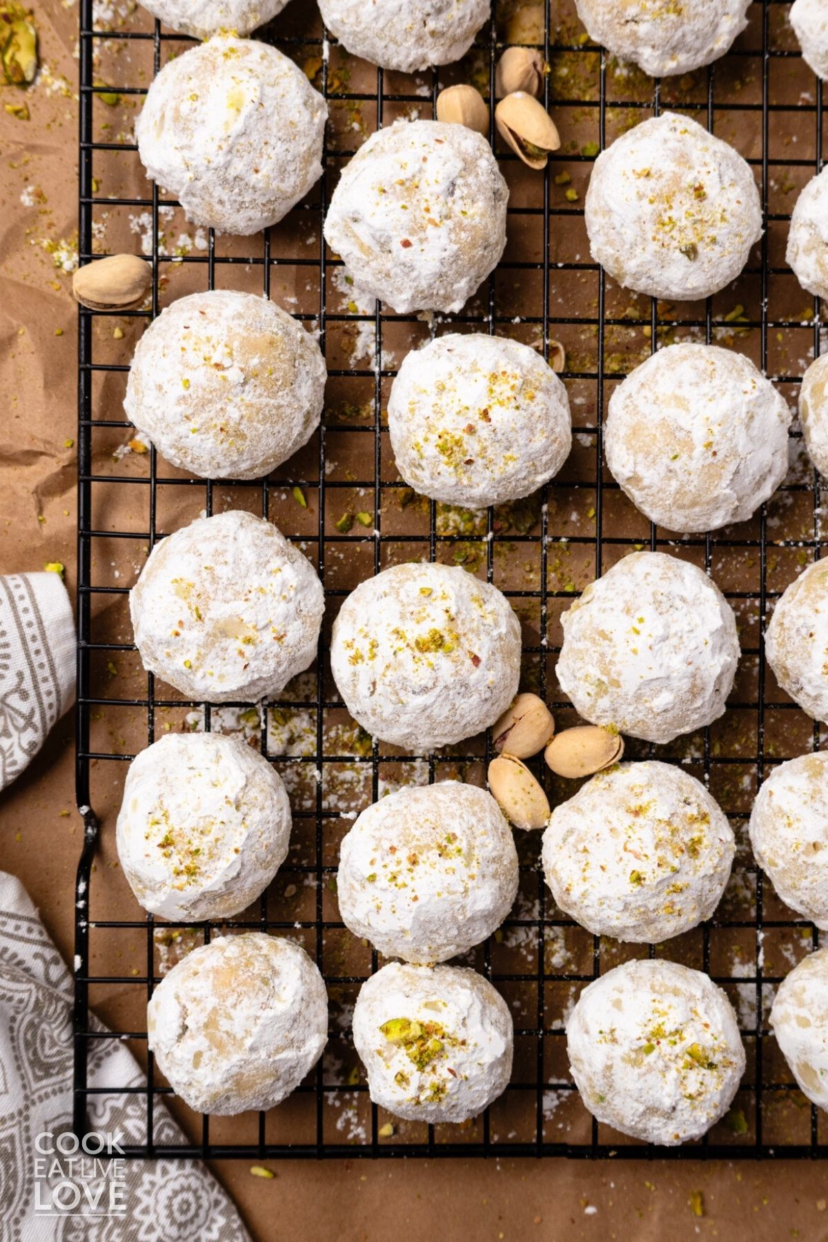 Pistachio snowball cookies on a wire cooling rack with pistachios in the shell sprinkled around.