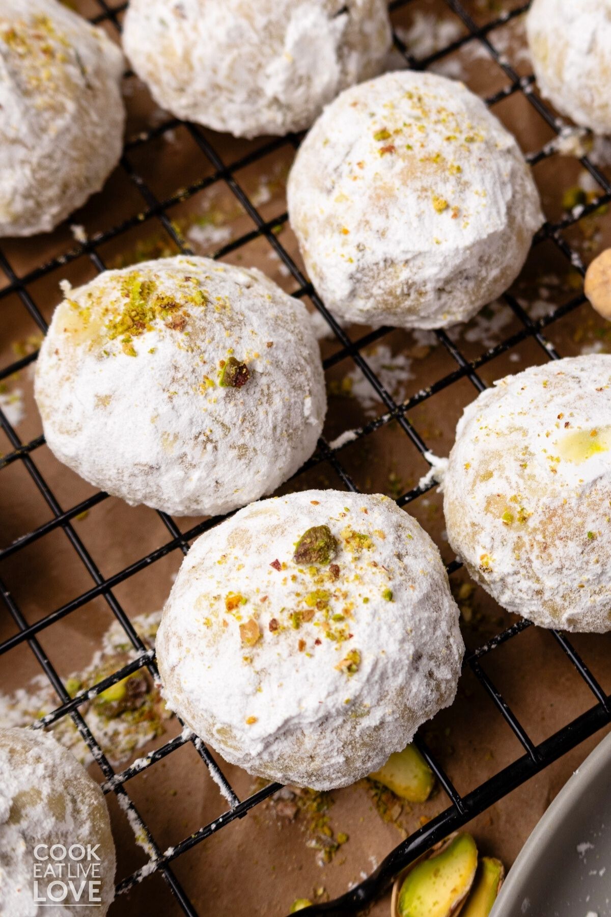 Pistachio snowball cookies rolled in powder sugar on a wire rack to cool. 