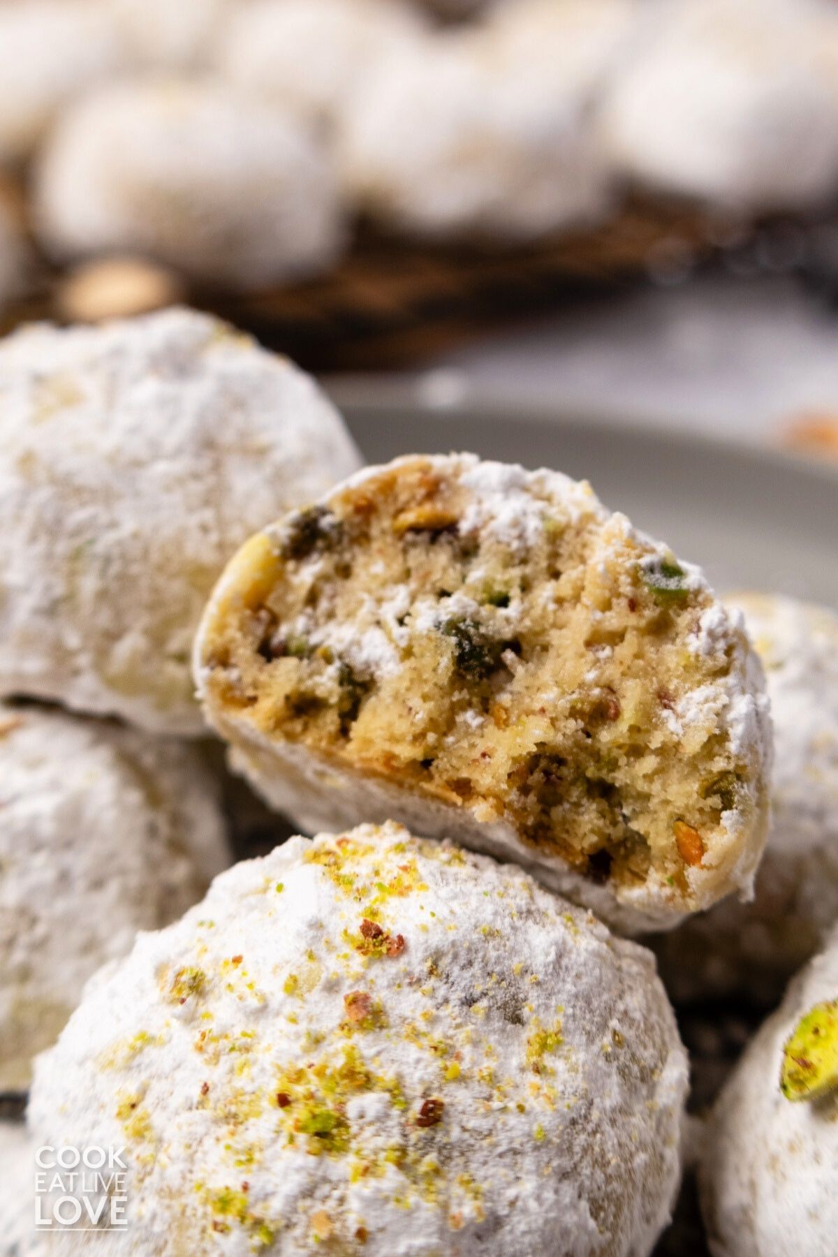 Pistachio snowball cookies in a pile with one missing a bite to show the inside. 