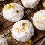 Pistachio snowball cookies coated in powdered sugar on a wire rack.