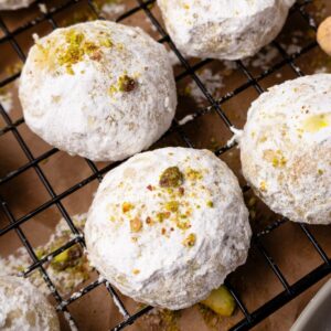Pistachio snowball cookies coated in powdered sugar on a wire rack.