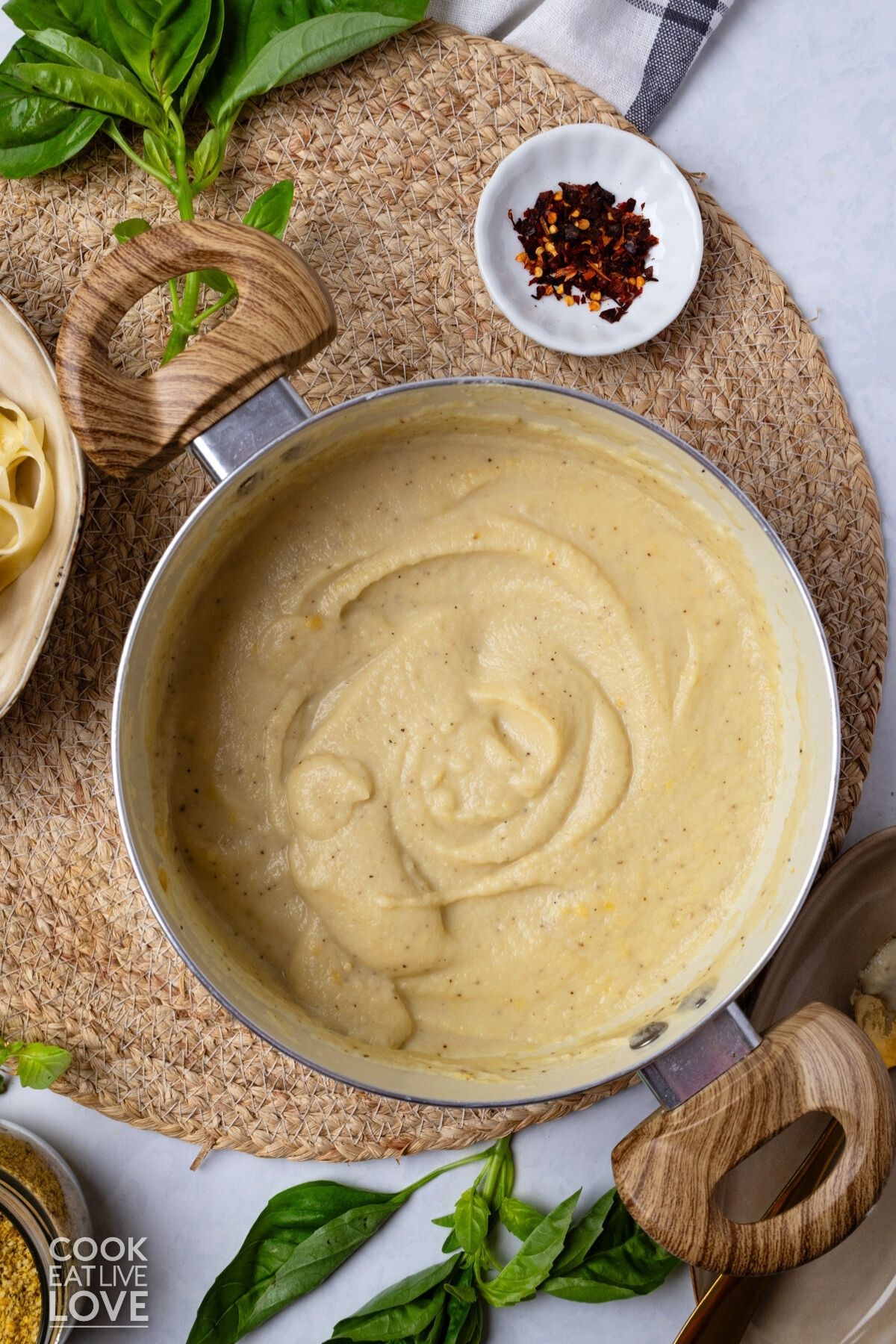Blended vegan alfredo in a pot with a plate of pasta to the side. 