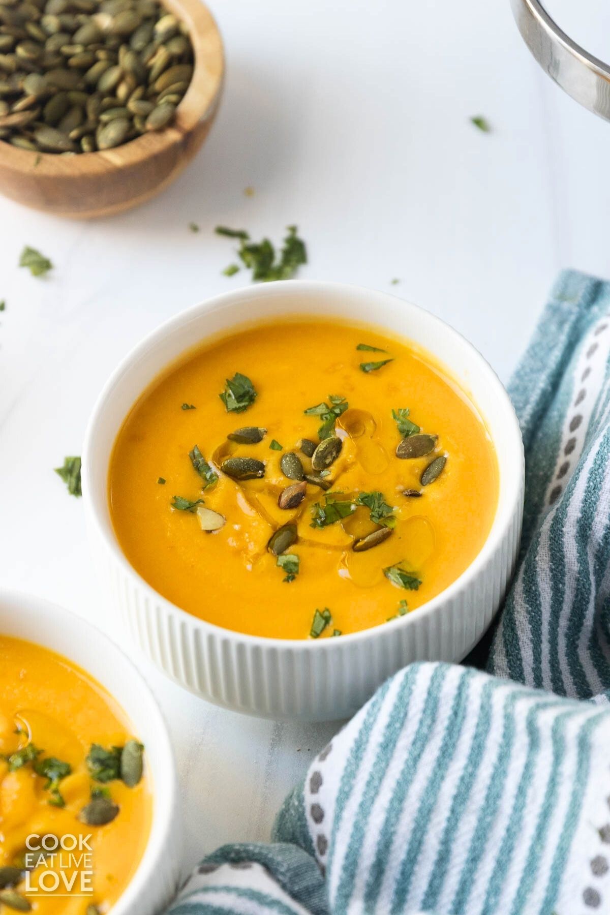 A bowl of butternut squash soup made with coconut milk on a table topped with pumpkin seeds and parsley.