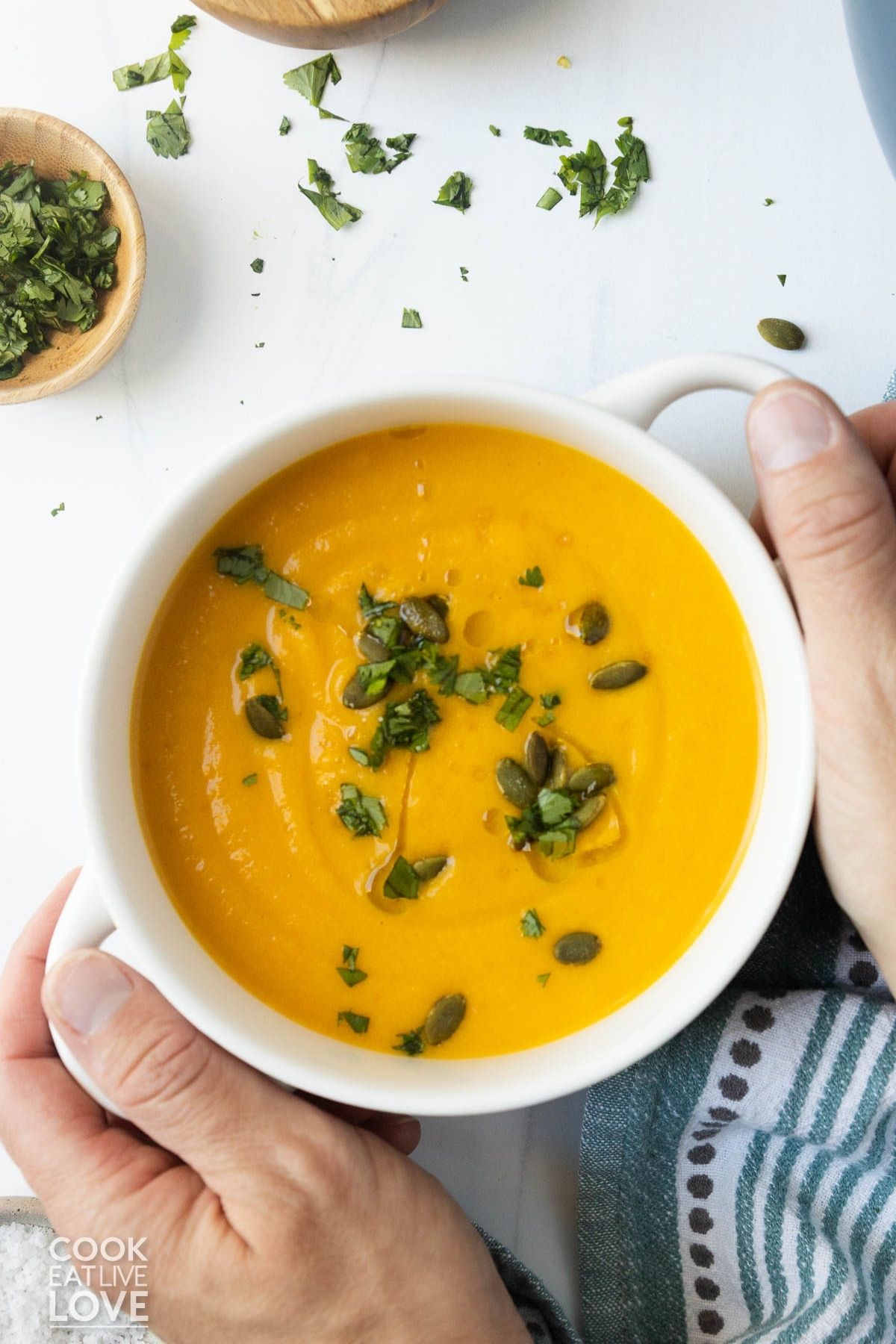 A bowl of butternut squash soup with coconut milk and hands around the edge of the bowl.