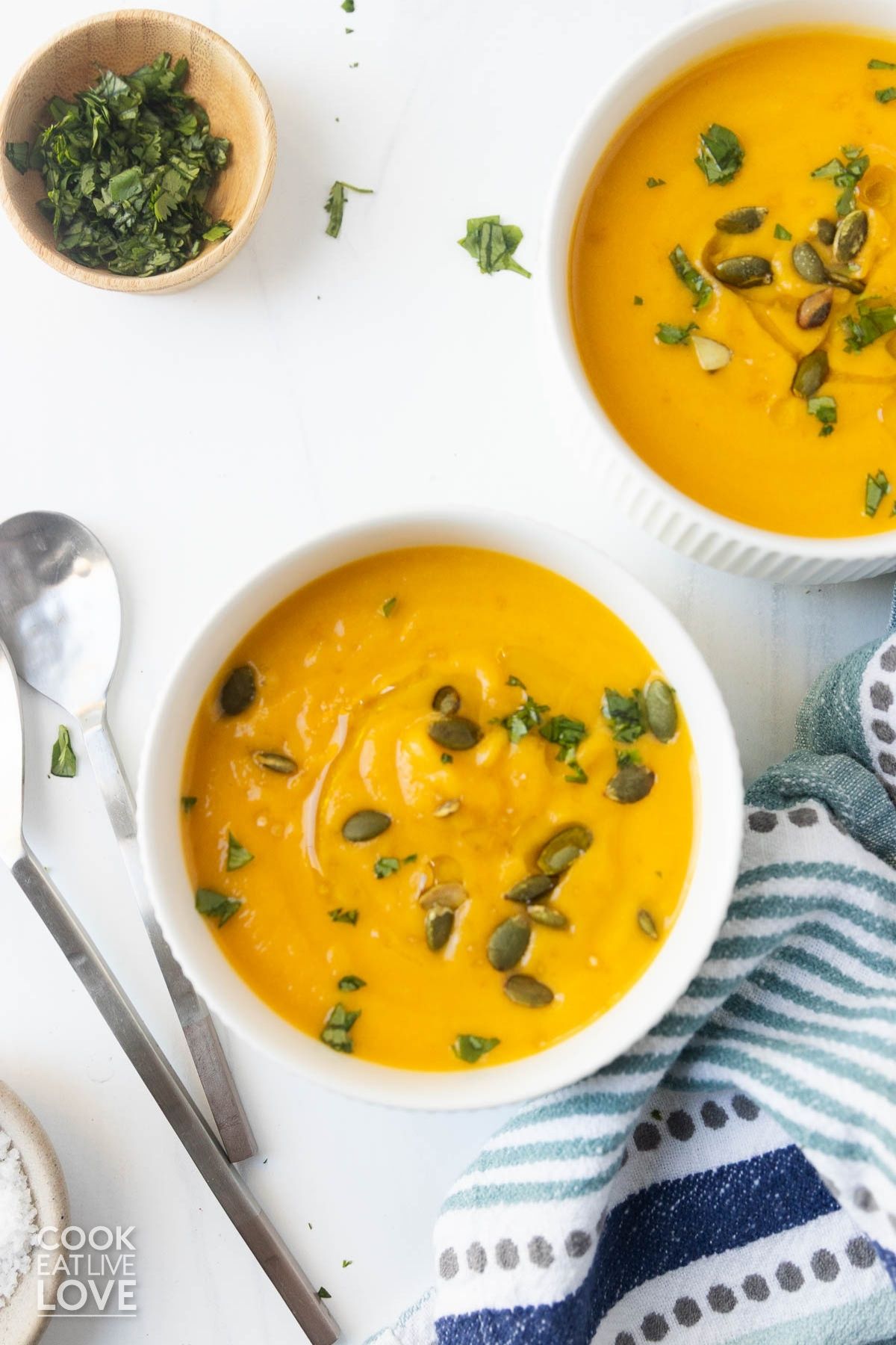 Bowls of butternut squash soup with coconut milk on a table with spoons to the side.