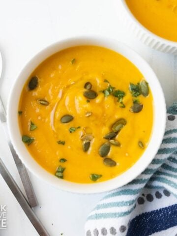 A white bowl of butternut squash soup with coconut milk garnished with pumpkin seeds.