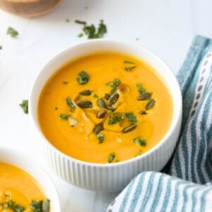 A bowl of butternut squash soup with coconut milk garnished with chopped parsley and pumpkin seeds.