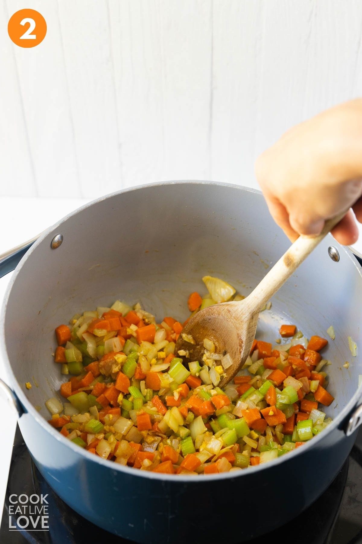 Garlic added to the pot and a hand stirring a wooden spoon.