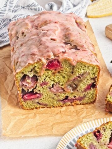 A loaf of matcha banana bread with strawberry glaze and a slice cut to show the inside.