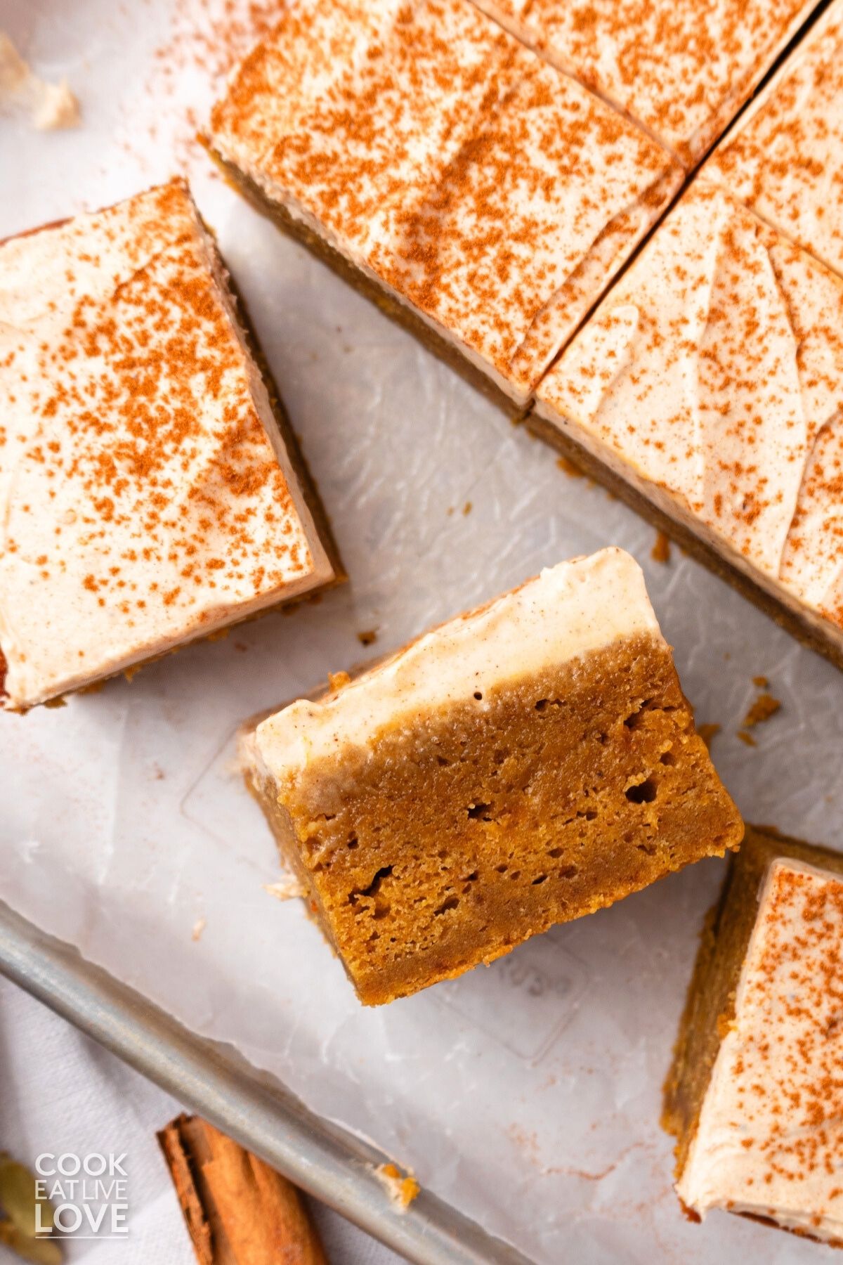 Pumpkin sheet cake on a baking tray with parchment and one sliced laying on its side. 