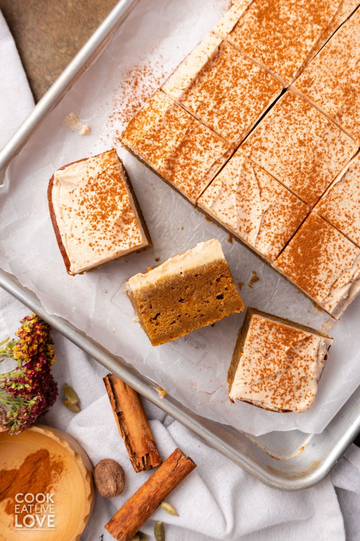 Pumpkin sheet cake with cream cheese frosting on a baking pan with a few slices pulled out and at different angles.