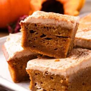 Slices of pumpkin sheet cake with chai cream cheese frosting stacked up in a pile.