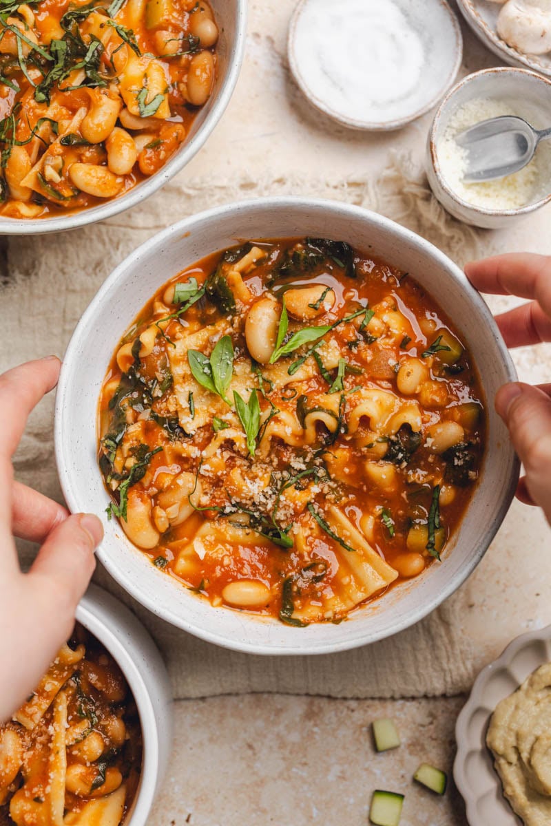 Hands grabbing a bowl of vegan lasagna soup on a table. 