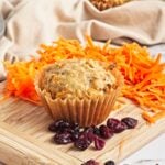 Carrot cake muffin on a wooden cutting board with shredded carrots in the background.