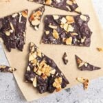Pieces of dark chocolate almond broke up and scattered on some parchment.
