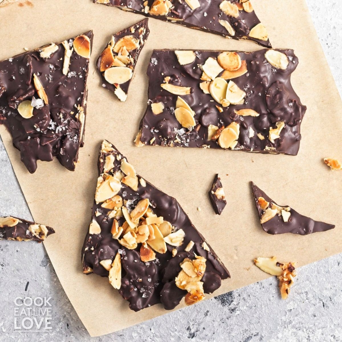 Pieces of dark chocolate almond broke up and scattered on some parchment.
