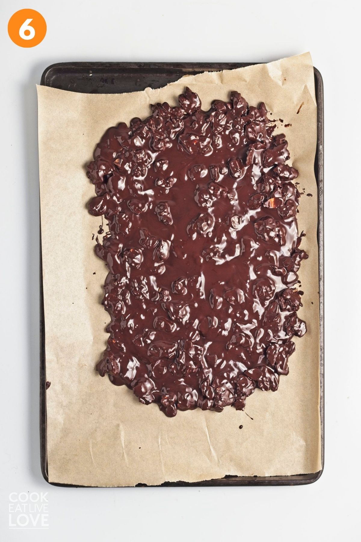 Melted chocolate with almonds spread out on a lined baking tray. 