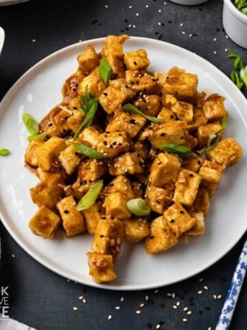 Honey garlic tofu on a white plate garnished with green onions.