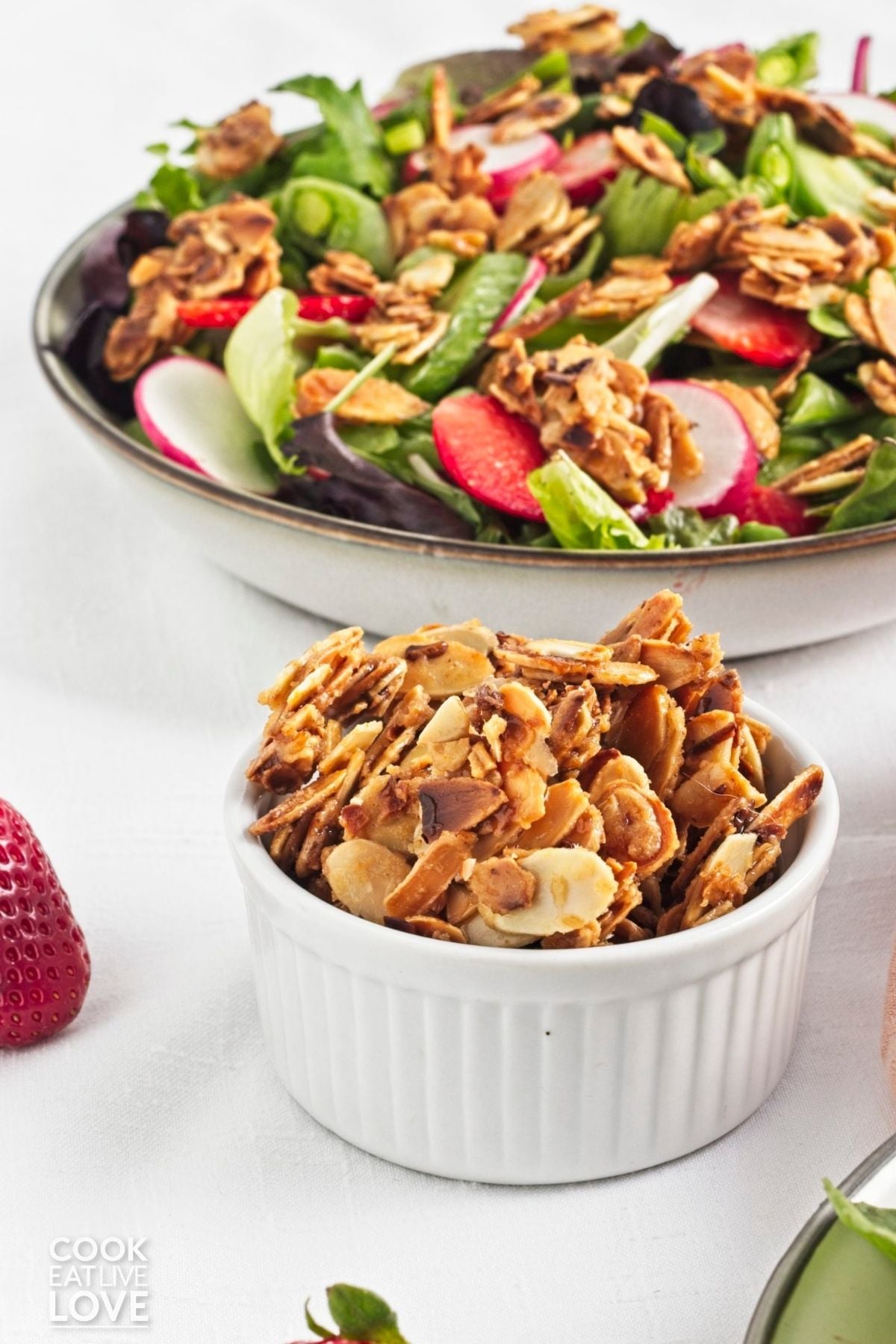 Spiced almonds in a white bowl in front of a salad. 