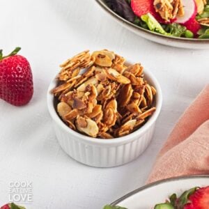 A white ramekin filled with spiced almonds on a table with a strawberry salad.