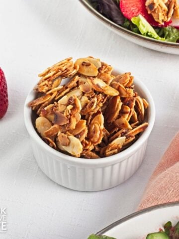 A white ramekin filled with spiced almonds on a table with a strawberry salad.