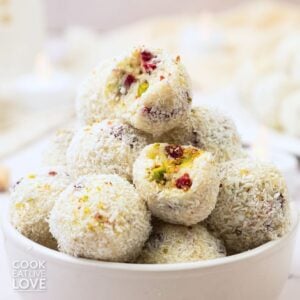 White chocolate truffles stacked in a bowl with a couple missing a bite to show the inside.