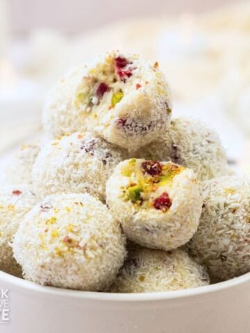 White chocolate truffles stacked in a bowl with a couple missing a bite to show the inside.