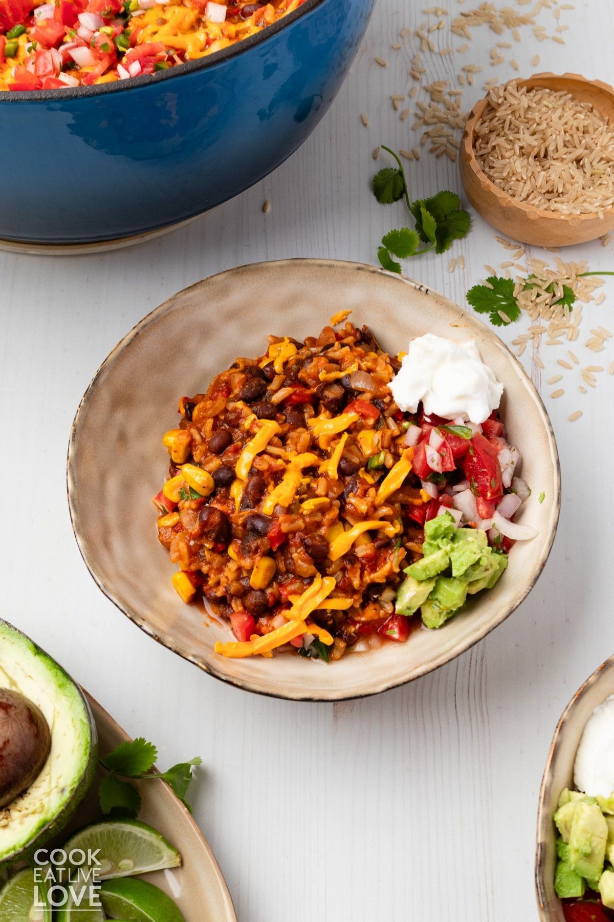 Taco rice with cheese on top in a bowl with a side of sour cream and guacamole.