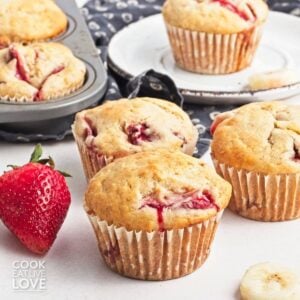 Strawberry banana muffins with fresh strawberries and banana slices around them.