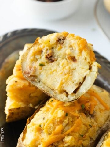 Vegan twice baked potatoes on a platter with one on top cut in half.