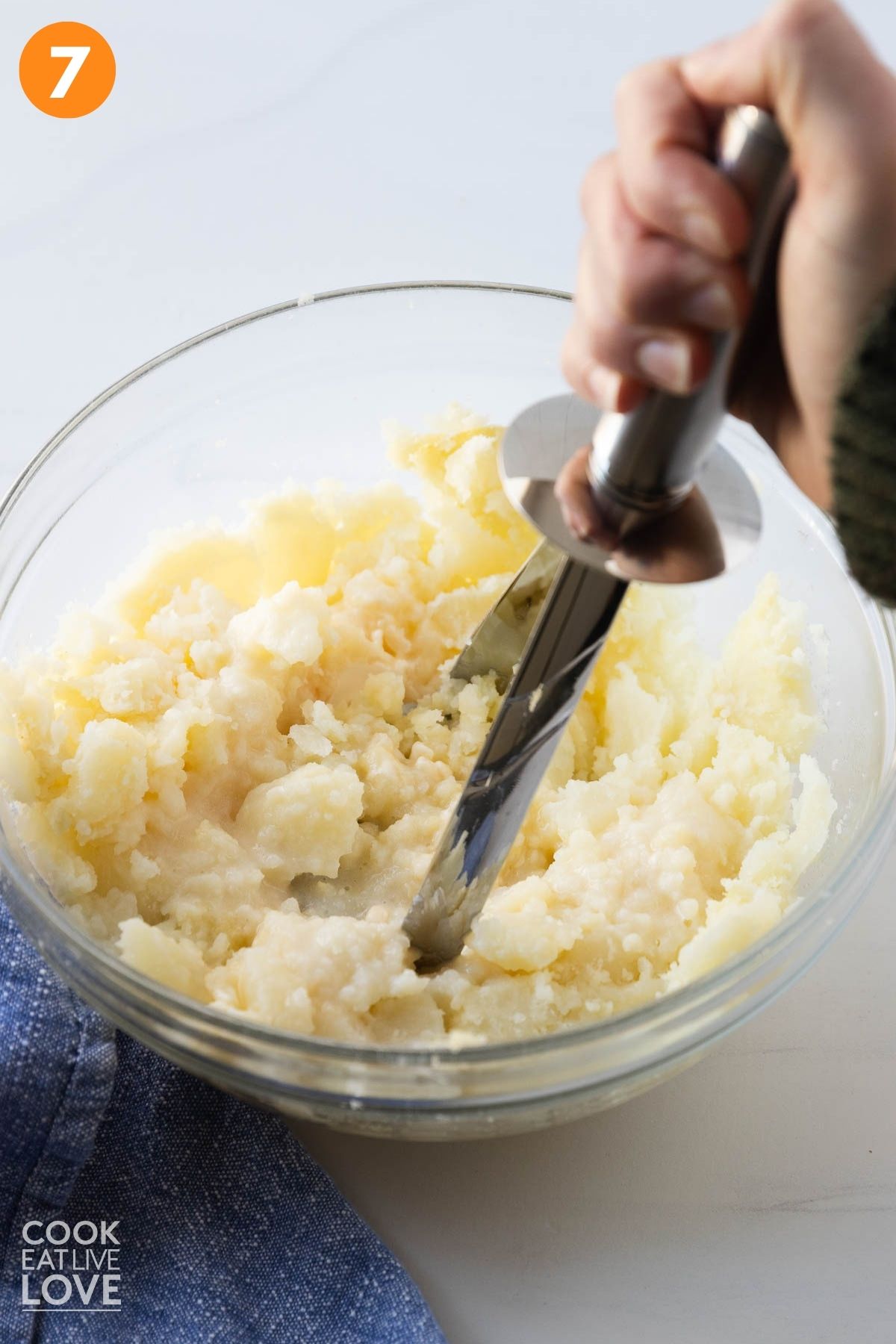 Using a hand masher to mash the potato.