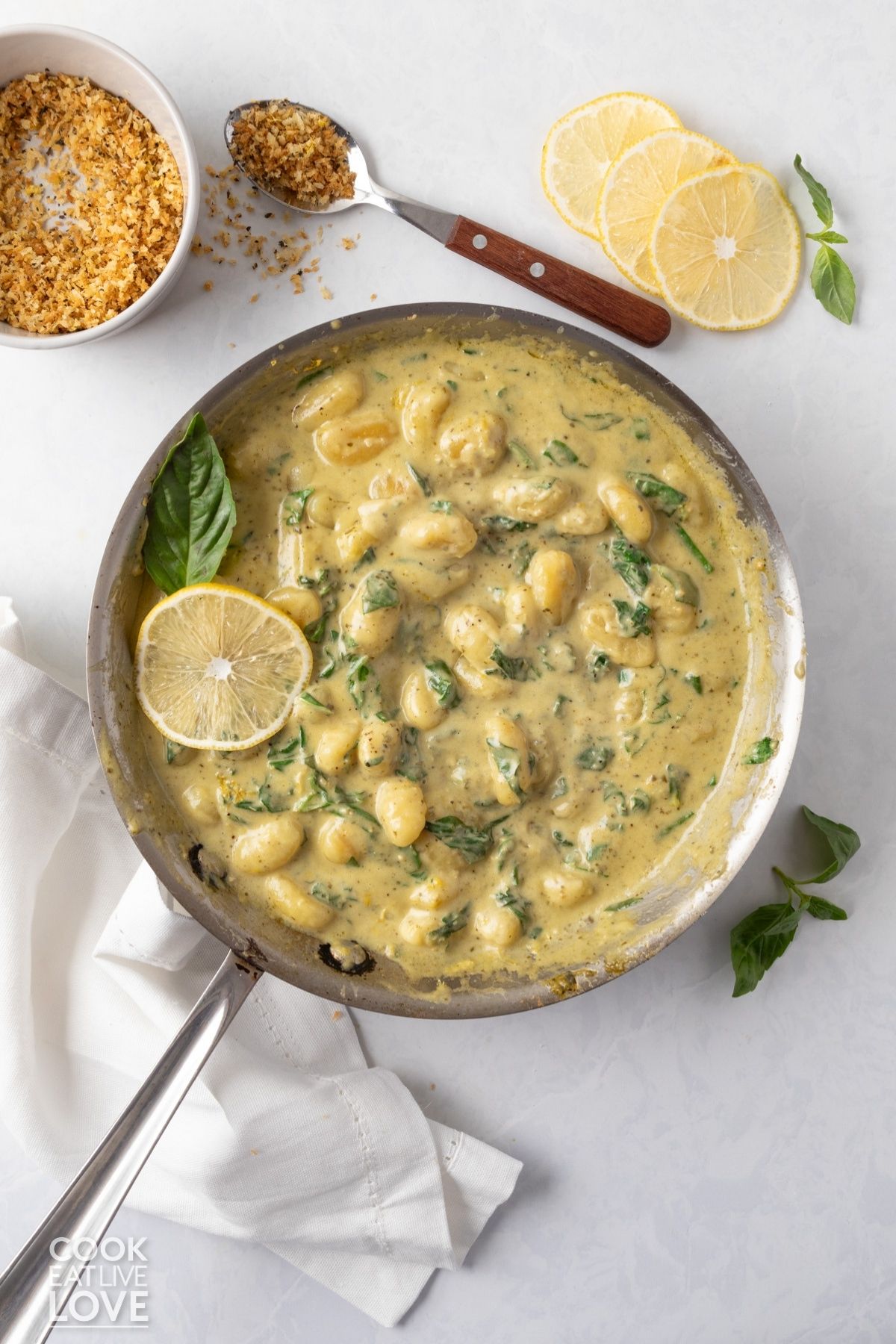 A skillet of creamy pesto gnocchi with basil and lemon.